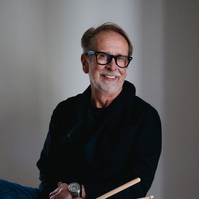 Ein Mann sitzt auf einer großen Trommel mit Drumsticks in der Hand