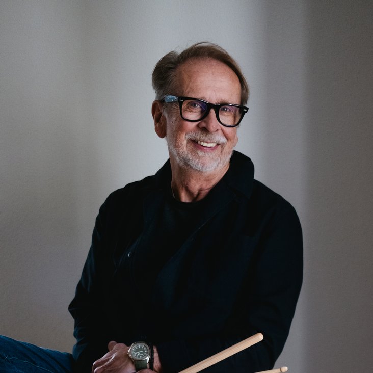 Ein Mann sitzt auf einer großen Trommel mit Drumsticks in der Hand