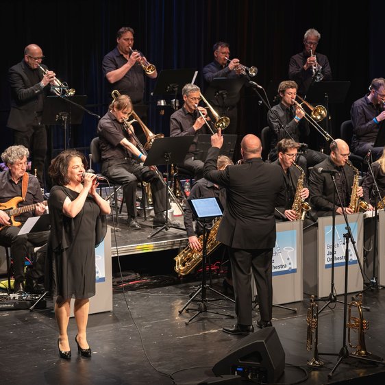 Big Band auf Bühne mit Sängerin vorne, Dirigent mittig, Schilder „Bosch Jazz Orchestra“.
