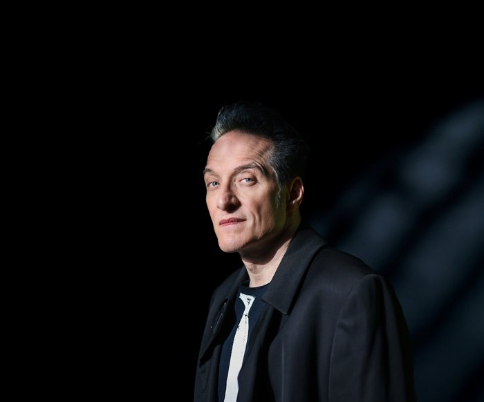 Ein Portrait des Musikers Bela B Felsenheimer. Er steht vor einer schwarzen Wand und trägt eine schwarze Jacke. Ein Lichtstrahl fällt auf ihn.