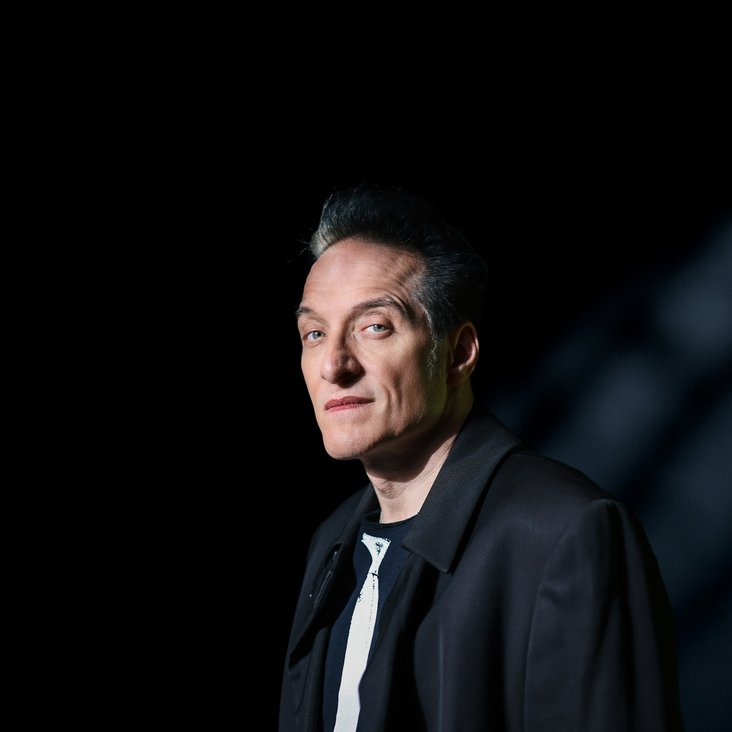 Ein Portrait des Musikers Bela B Felsenheimer. Er steht vor einer schwarzen Wand und trägt eine schwarze Jacke. Ein Lichtstrahl fällt auf ihn.