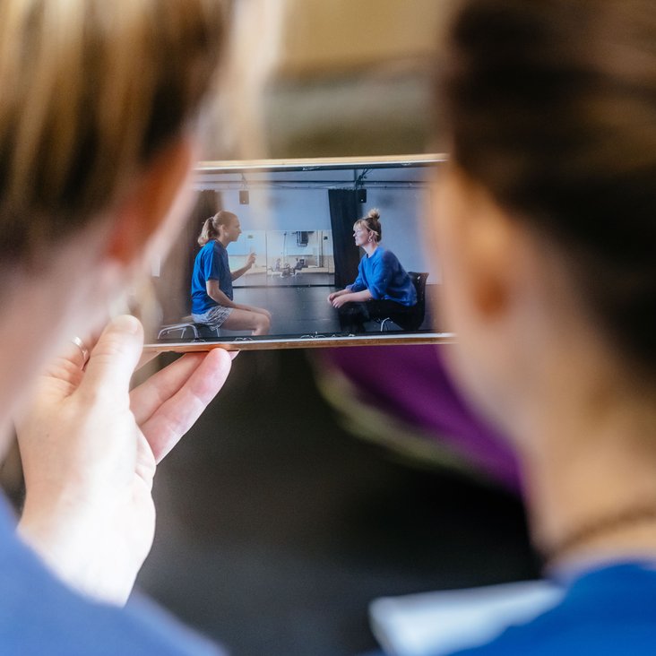 Zwei Köpfe von hinten, die in ein Smartphone schauen. Auf dem Smartphone sehen Sie sich ein Video an